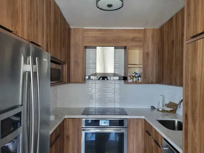 Cocina moderna completa con gabinetes de madera cálida, azulejos blancos tipo metro, electrodomésticos de acero inoxidable, encimeras de granito e isla con estufa