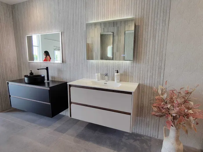Modern bathroom showroom display featuring two contemporary vanity units with black and white cabinetry, backlit mirrors, vertical shiplap wall paneling, and designer accessories.