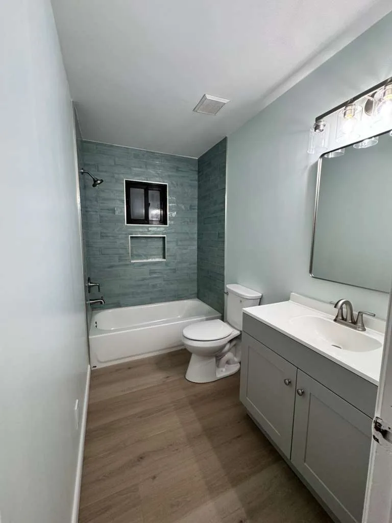 Modern bathroom with slate-tiled shower enclosure, white vanity with integrated sink, and wood-look flooring