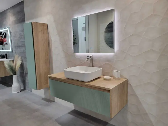 Modern bathroom vanity display with white vessel sink, wood and sage green cabinet, geometric tile backsplash, and LED mirror in showroom