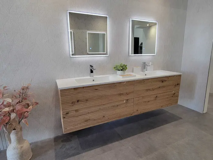 Completed modern bathroom vanity with dual sinks, illuminated mirrors, and wood-grain cabinetry against textured gray tile walls.