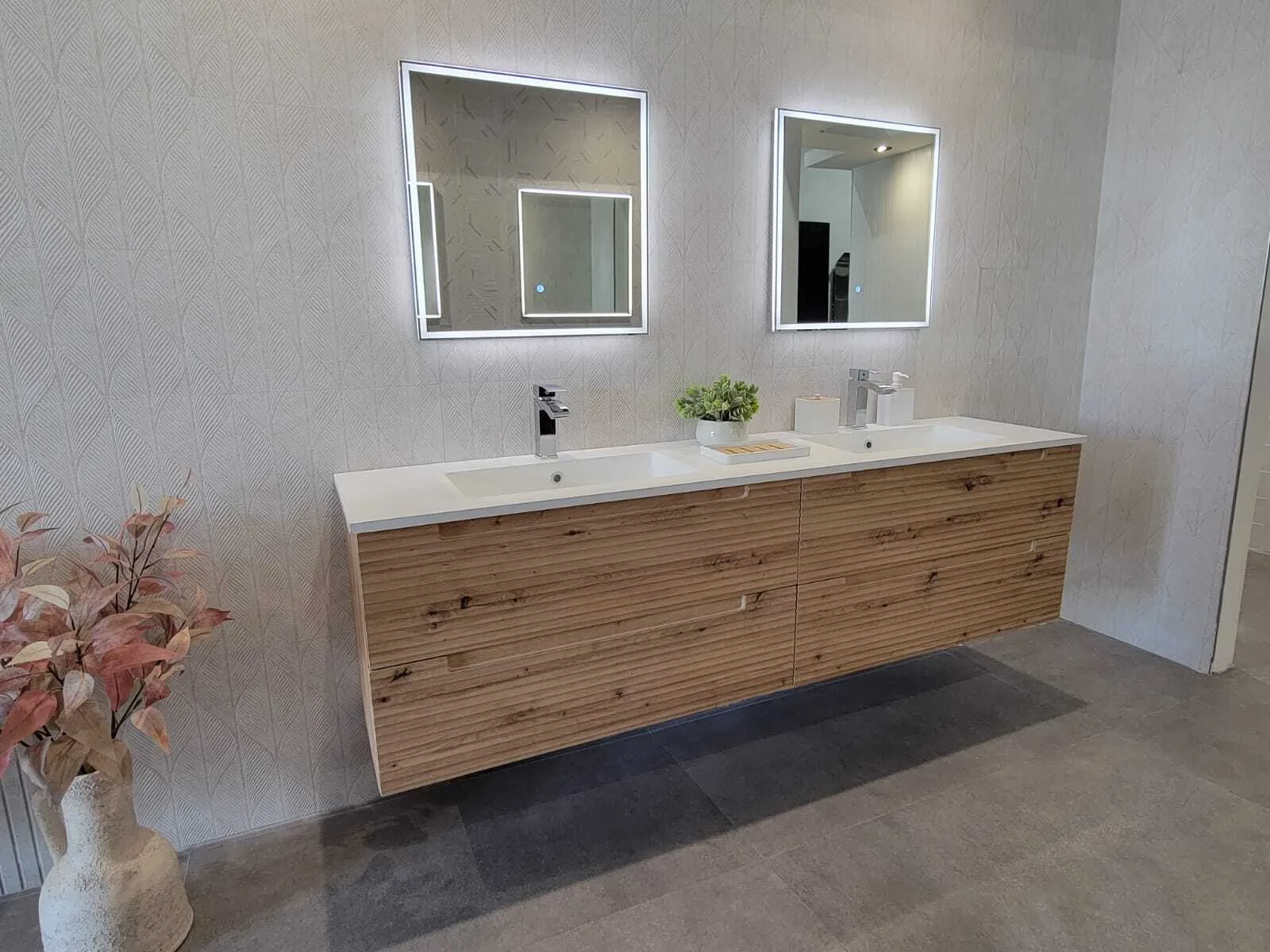 Completed modern bathroom vanity with dual sinks, illuminated mirrors, and wood-grain cabinetry against textured gray tile walls.