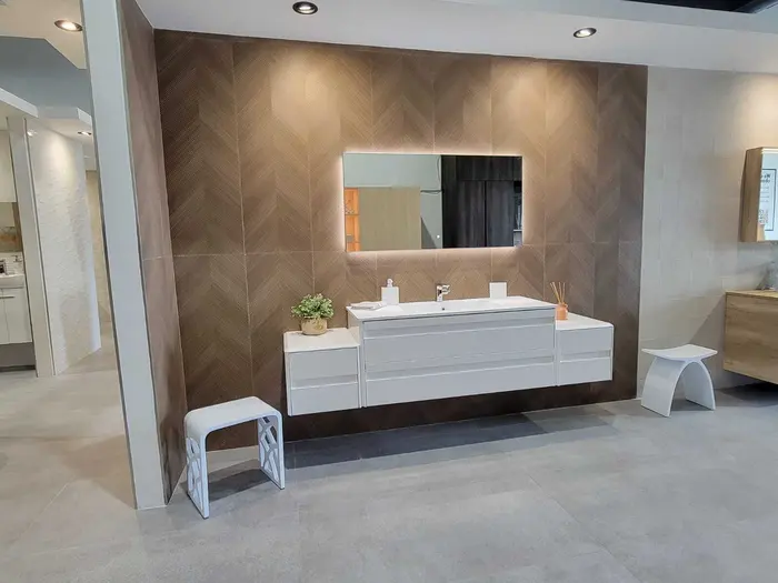 Bathroom vanity showroom display featuring multiple modern white and wood-tone sink vanities with herringbone tile backsplash and illuminated mirror