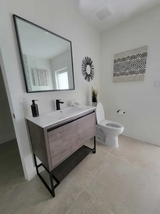 Modern finished bathroom with floating wood vanity, white quartz countertop, contemporary black-framed mirror, white toilet, and geometric wall art on clean white walls