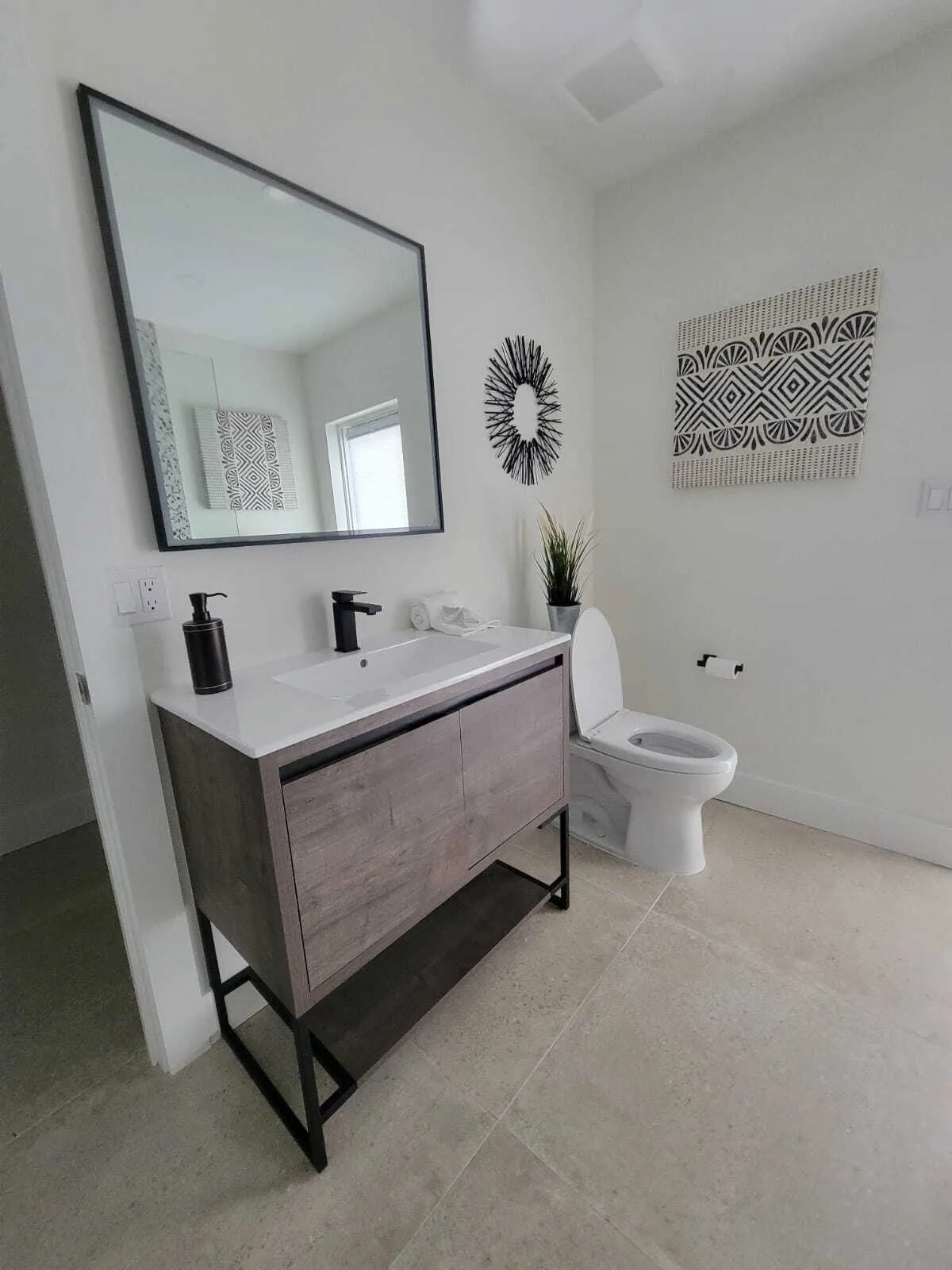 Modern finished bathroom with floating wood vanity, white quartz countertop, contemporary black-framed mirror, white toilet, and geometric wall art on clean white walls