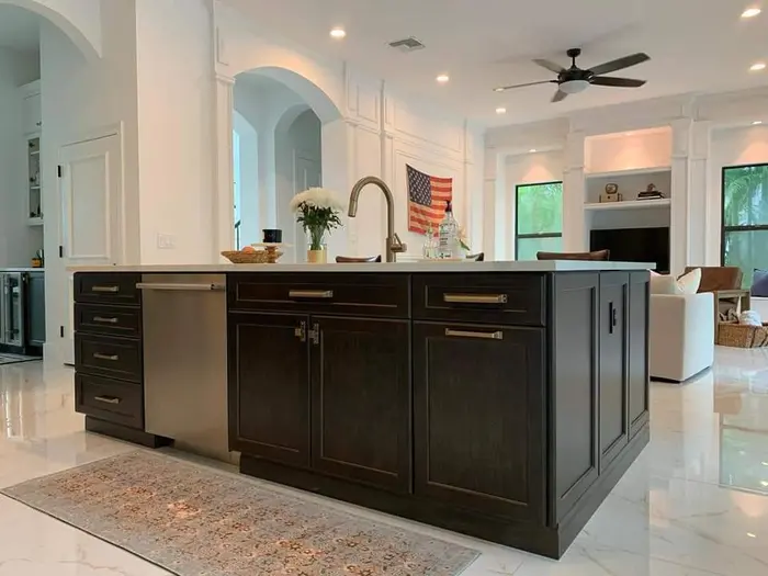Completed modern kitchen with dark cabinetry, waterfall island countertop, pendant lighting, and open-concept living space