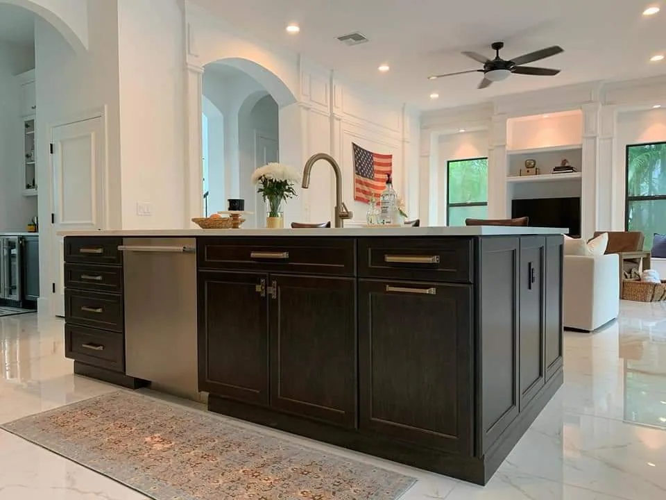 Completed modern kitchen with dark cabinetry, waterfall island countertop, pendant lighting, and open-concept living space