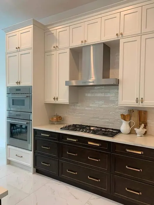 Modern kitchen with two-tone cabinetry featuring cream upper cabinets and black lower cabinets, stainless steel range hood, gas cooktop, subway tile backsplash, and marble countertops with integrated appliances.