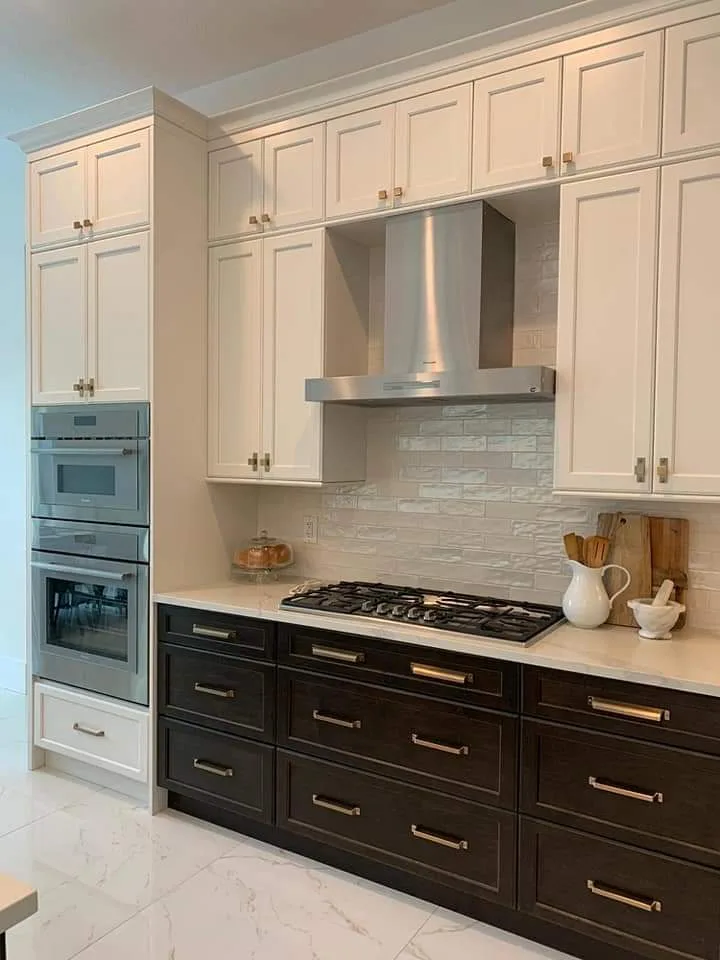 Modern kitchen with two-tone cabinetry featuring cream upper cabinets and black lower cabinets, stainless steel range hood, gas cooktop, subway tile backsplash, and marble countertops with integrated appliances.