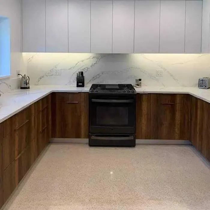 Completed modern kitchen with warm wood cabinetry, white marble backsplash with under-cabinet lighting, white quartz countertops, and black gas range.