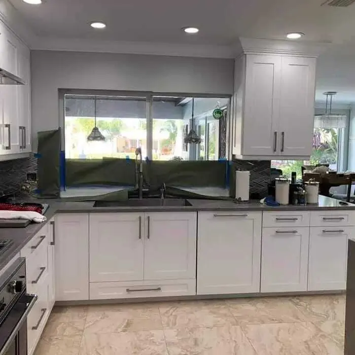 Completed modern kitchen with white painted cabinets, black countertops, marble tile flooring, large sliding glass doors with garden views, and recessed ceiling lighting
