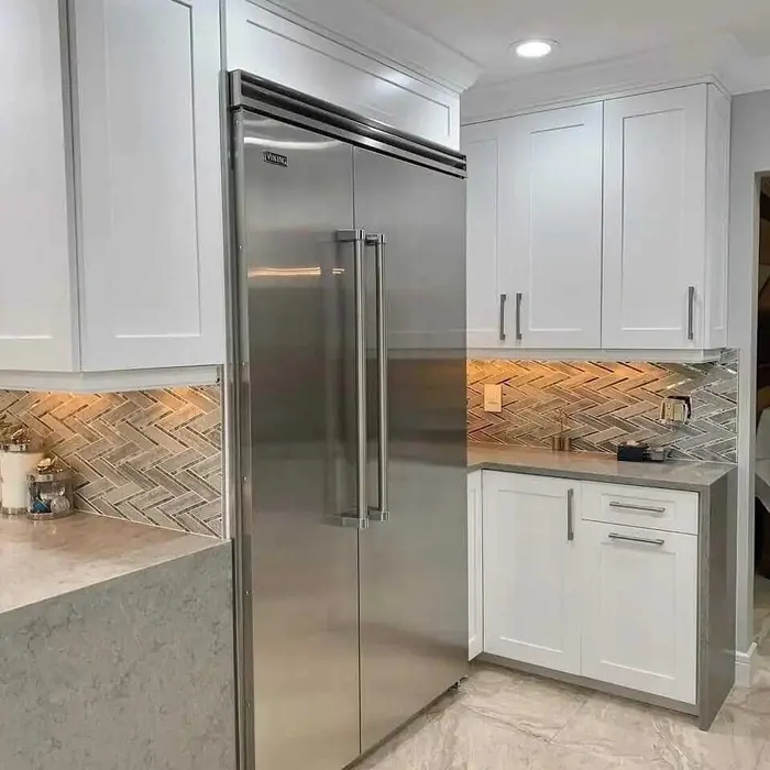 Modern kitchen with white painted cabinets, herringbone wood-look backsplash, stainless steel Viking refrigerator, and gray quartz countertops in a completed residential remodel.