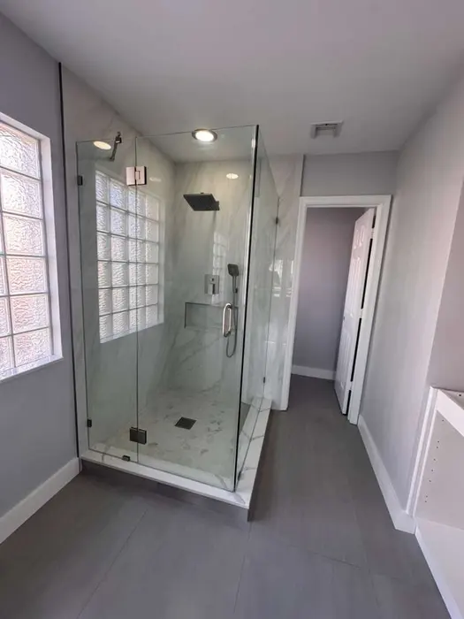 Completed luxury bathroom with marble-tiled walk-in shower enclosure, frameless glass doors, dark tile flooring, and custom glass block window feature