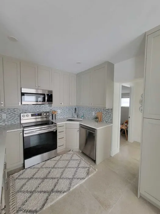 Newly remodeled kitchen with cream-white shaker cabinetry, mosaic glass tile backsplash, stainless steel appliances, granite countertops, and polished tile flooring in a residential home